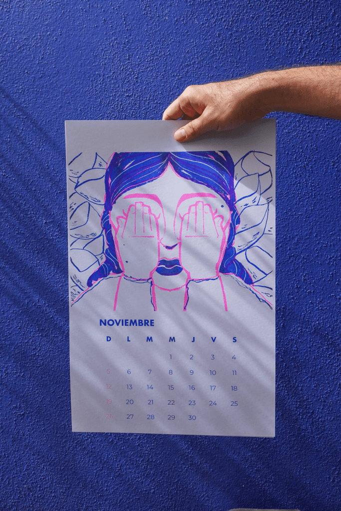 A hand holding a colorful November calendar featuring an illustration of a woman covering her eyes, with a purple background.
