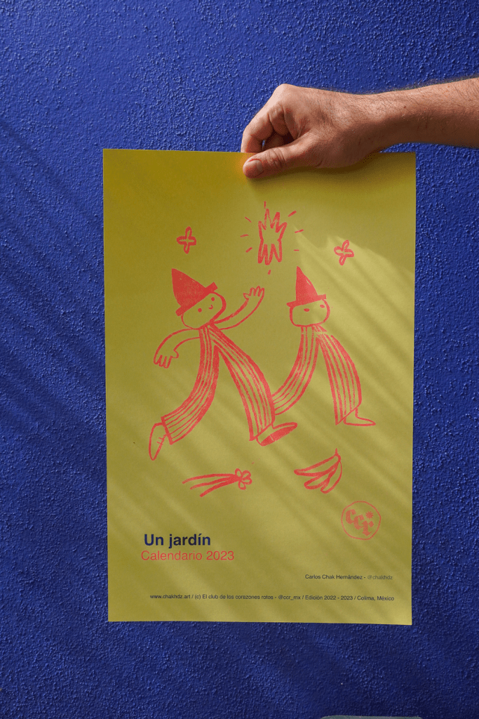Un hombre sostiene un calendario amarillo titulado 'Un jardín' con ilustraciones de dos figuras con sombreros de mago. El fondo es de color azul.