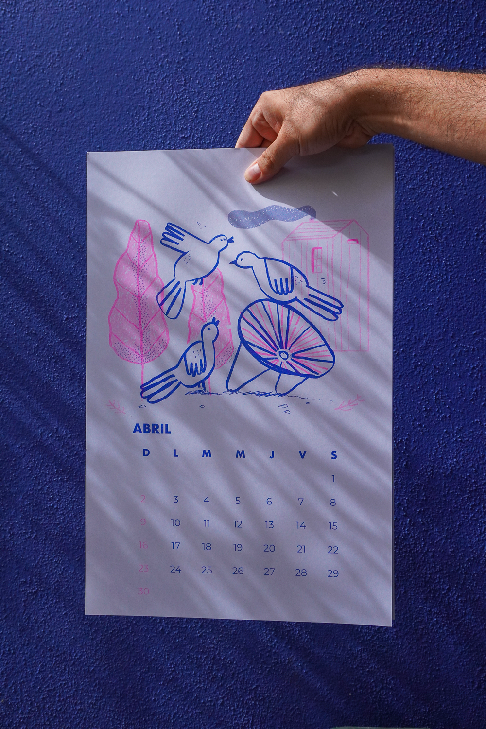 A person holding a colorful April calendar featuring illustrations of birds and plants against a blue textured background.