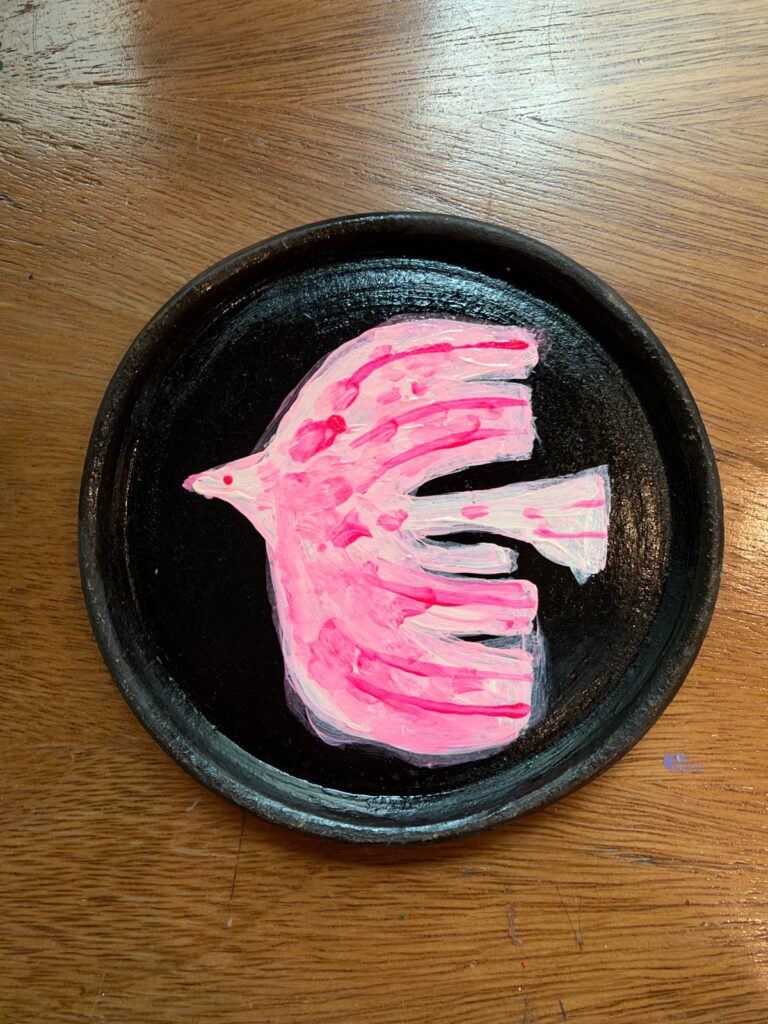 Pájaro en vuelo pintado en acrílico rosa magenta sobre plato de barro negro oaxaqueño